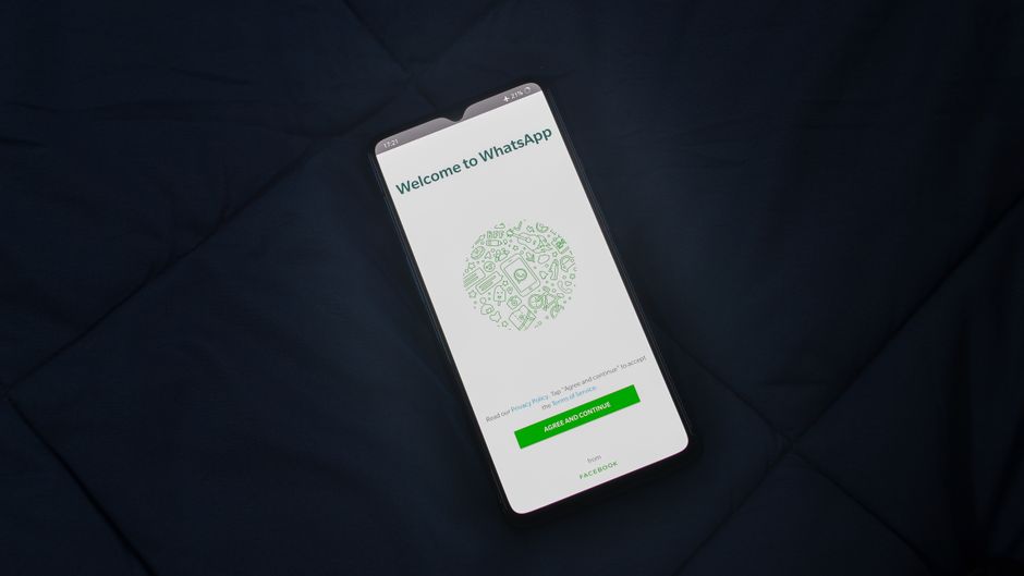 Smartphone displaying WhatsApp login screen on a dark surface. Overhead view.