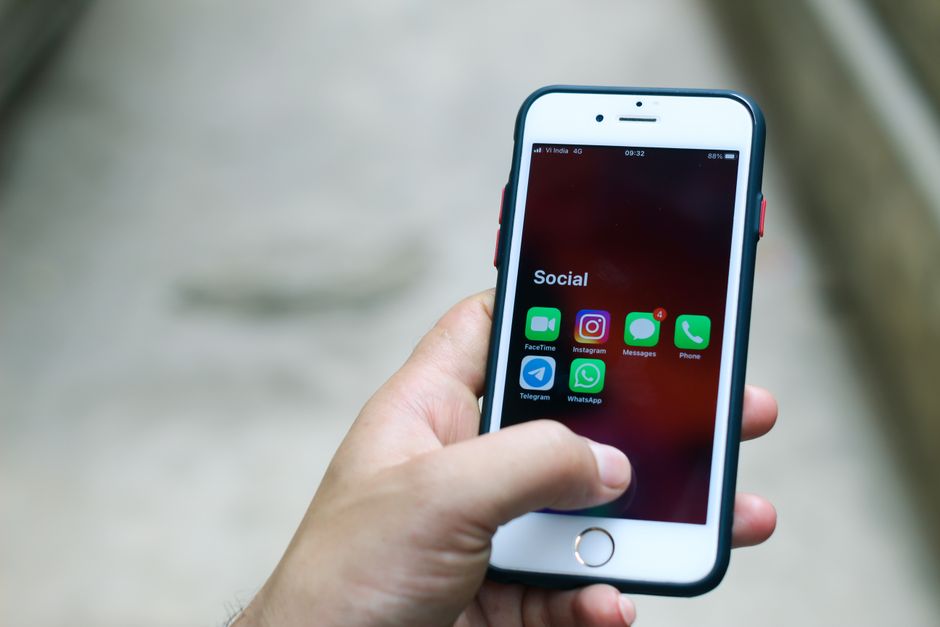 Hand holding a smartphone displaying various social media and communication apps.
