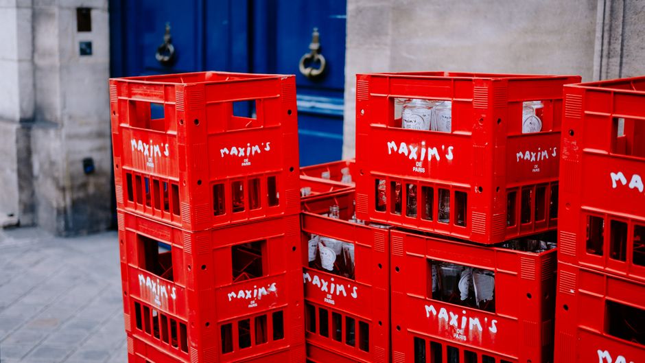 Red Maxim's de Paris crates stacked on a sidewalk, showcasing Parisian street scene.