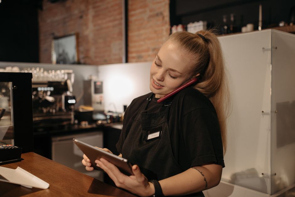 Young woman in café multitasks with a tablet and phone at the counter.