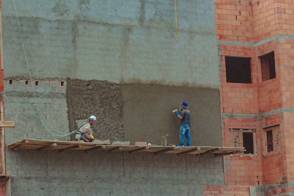 Painéis de andaime em construção com operários trabalhando, monitorados por um tablet com WhatsApp aberto.